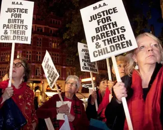 Women hold protest signs reading "Justice for birth parents and their children" at a nighttime gathering