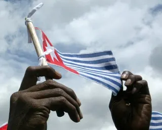 Hands holding aloft a small flag with a white star on a red background and blue and white stripes