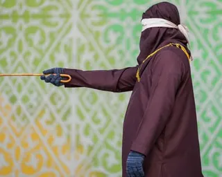 Person stands in hooded outfit holding cane