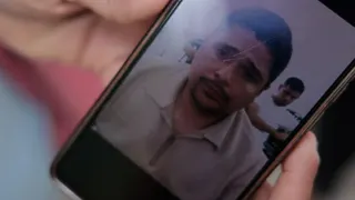 A phone displays the photo of a man in a beige zip up sweater