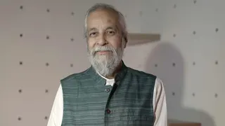 Madan Lokur is stood in a room with white walls, looking at the camera. He is wearing a sleeveless jacket over a white top and has grey hair and a grey beard.