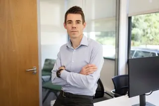 Sexton in office with computer screen, arms folded