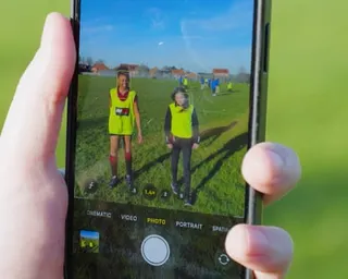 Closeup of hand holding smartphone showing image of two children in hi-vis vests.