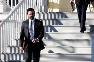 a man in a suit walks out of a residence while carrying a folio