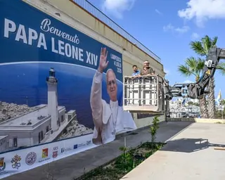 Workers in a cherrypicker next to a large banner with an image of Pope Leo