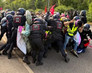 Riot police in helmets surround and push against a group of protesters on a road