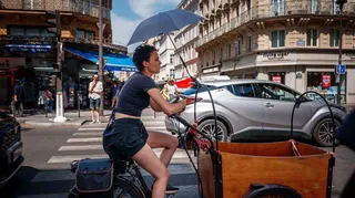A woman protects herself from the sun under an umbrella as she rides a bicycle in Paris on June 25, 2026, as France experiences a heatwave.