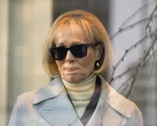 a woman in a coat, turtleneck and sunglasses looks to the side