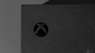 close-up of the Xbox power button on an Xbox Series X video game console photographed on a dark gray background