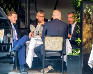 The three men sitting at a table outdoors with another man whose back is to the camera