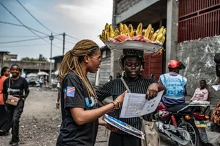 GOMA, DEMOCRATIC REPUBLIC OF CONGO - JUNE 24: A woman carrying plantains reads a pamphlet as workers with UNICEF's 'U-Report' group raise awareness about Ebola transmission at Alanine market on June 24, 2026 in Goma, Democratic Republic of Congo. On Monday, UN agencies announced that Ebola cases in the Democratic Republic of Congo had surpassed 1,000. Although testing capacity has recently improved, surveillance and contact tracing remain constrained by insecurity and restricted access in Ituri 