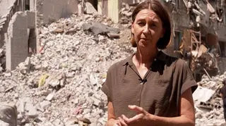 Sarah Rainsford in a brown shirt with short sleeves in front of rubble in Kyiv