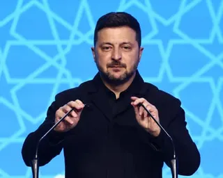 Zelenskyy holds two microphones that are placed on a lectern, as he speaks against a blue backdrop
