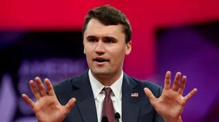 Charlie Kirk gestures with his hands as he talks in front of a red and purple background