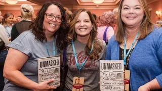 Three women wearing lanyards hold up a true-crime book