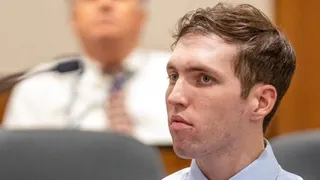 A man with short wavy brown hair and beard stubble looks forward almost expressionless (file picture)