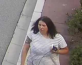 Anastasiia Berezovska with dark hair in a striped shirt walks on a pavement while holding a phone
