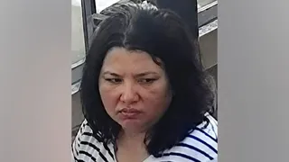A woman with dark hair and a serious expression looks down. She wears a striped black and white shirt.