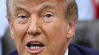 US President Donald Trump has his mouth open in a close up shot. His eyebrows are raised and he is wearing a blue suit jacket.
