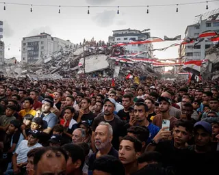 Egyptian flag fly over a large crowd of people, some of them in the background standing on the rubble of a destroyed building