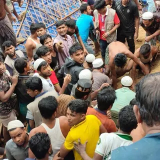 A large crowd gathers around a muddy site as people work by hand to try to rescue people from under the mud
