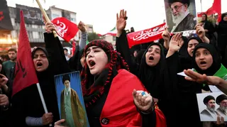 Mourners shout slogans on the day of a funeral procession for Iran's late Supreme Leader Ayatollah Ali Khamenei. In shot is a group of  women holding photos of  Khamenei. The lady in the centre is wearing red and black and shouting