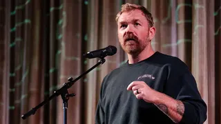 Graham Platner wearing a sweatshirt and speaking into a mic