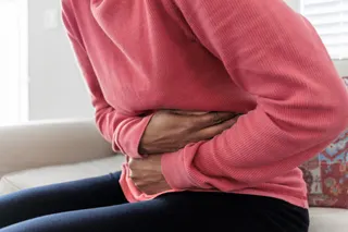 Close-up of unrecognizable black woman sitting on couch holding her abdomen in pain.