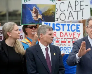 a man in a suit and tie in front of a crowd with signs