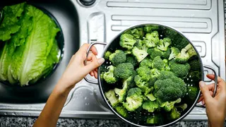 A person prepares broccoli in a kitchen.