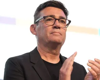 Burnham in black-rimmed glasses and a black blazer gestures with both hands while speaking