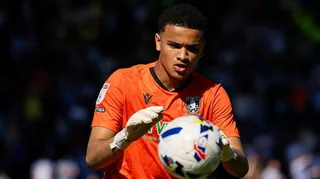 Pierce Charles concentrates on catching the ball in his hands, wearing orange goalkeeping jersey