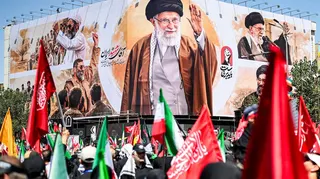 Crowds with Iranian flags in front of a billboard showing the late suprememe leader at his funeral