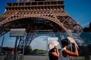 Two tourists shade themselves with fans as they walk past the base of the Eiffel Tower