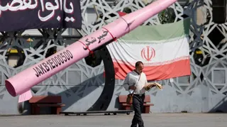 A man walks next to a symbolic mockup of an Iranian missile and an Iranian flag at Imam Hussein Square in Tehran, Iran, July 12, 2026.