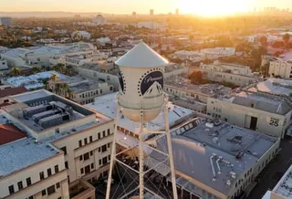 An aerial view of a white water tower with the Paramount logo at Paramount Studios, surrounded by buildings at sunset