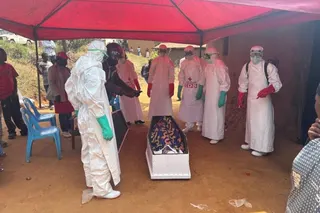 A burial team in full protective gear prepares a coffin.