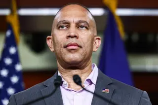 Hakeem Jeffries speaks at a microphone podium in a dark suit and light purple shirt