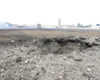 Closeup of a crater in the runway, with emergency vehicles in the distance
