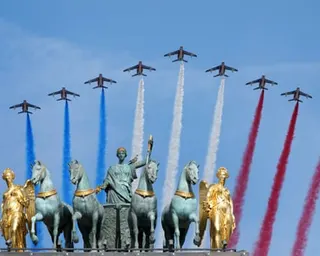 Jets with red, white and blue smoke trails fly over a group of statues