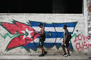 Two young men walk past a wall depicting a Cuban flag during a widespread blackout in Havana on July 14, 2026.