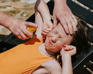 A little girl grimaces as a parent applies sunscreen.