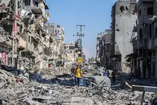 A street in Khan Yunis, Gaza filled with rubble and destroyed buildings, with people walking through debris