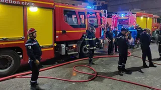 Firefighters in blue uniforms stand in front of fire trucks