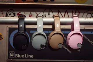 Four versions of Skullcandy’s Crusher 1080 ANC headphones hanging on a subway train handlebar.