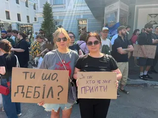 Two young protesters hold up signs reading "What are you doing, you idiot?" and "This is for all of those who couldn't be here"