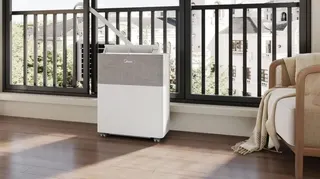 A Midea PortaSplit by the window of an apartment, with a tube connecting the indoor and outdoor units