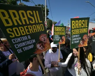 Protesters hold large green signs with yellow text and images of political figures at a street demonstration
