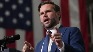 JD Vance wearing a suit and speaking into a microphone in front of an American flag