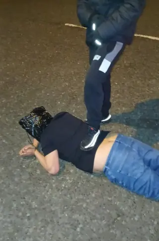 Many lying on the floor with a bag over his head and another man with his foot on his back